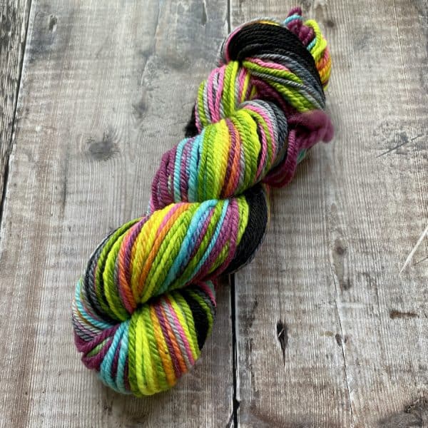 Glorious squishy, bright neon yarn in multicolour on wooden background. Worsted weight, hand spun by Eleanor Shadow in the UK