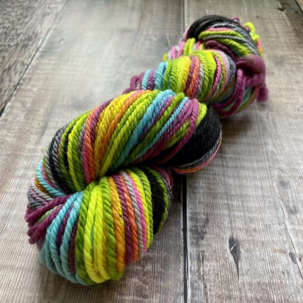 Multicolour neon Worsted weight hand spun yarn on a wood background. Hand spun by Eleanor Shadow.