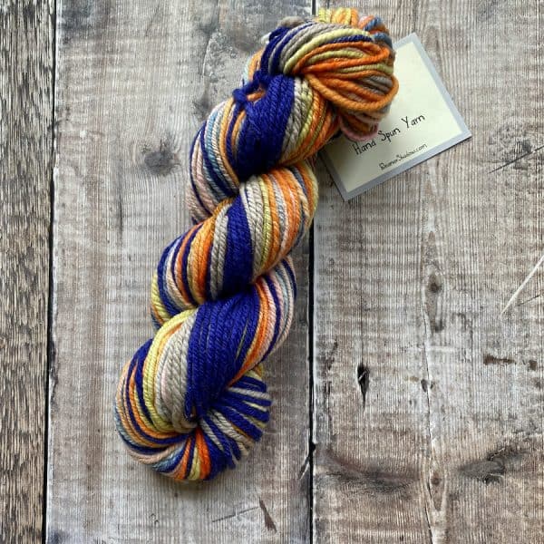 Blue, pink, orange and yellow hand spun yarn on wood background, by Eleanor Shadow