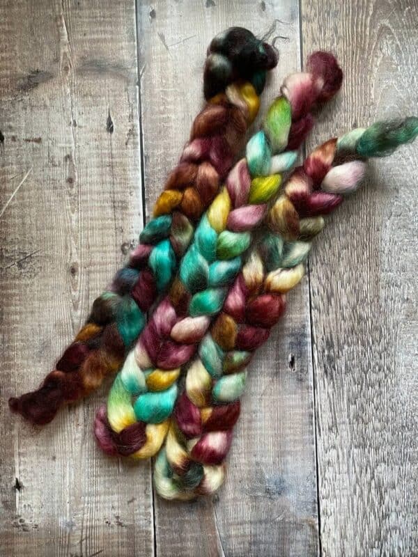 Three braids of Wensleydale wool top in Autumn jewel tones, flat lay on wood table
