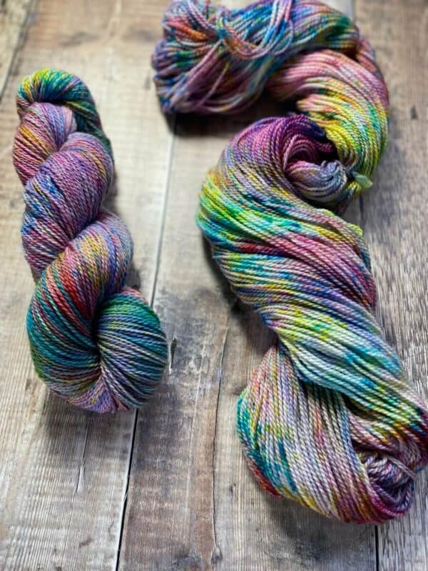 Two skeins of She Blooms, a variegated jewel tone yarn in multicolours, on a wood table