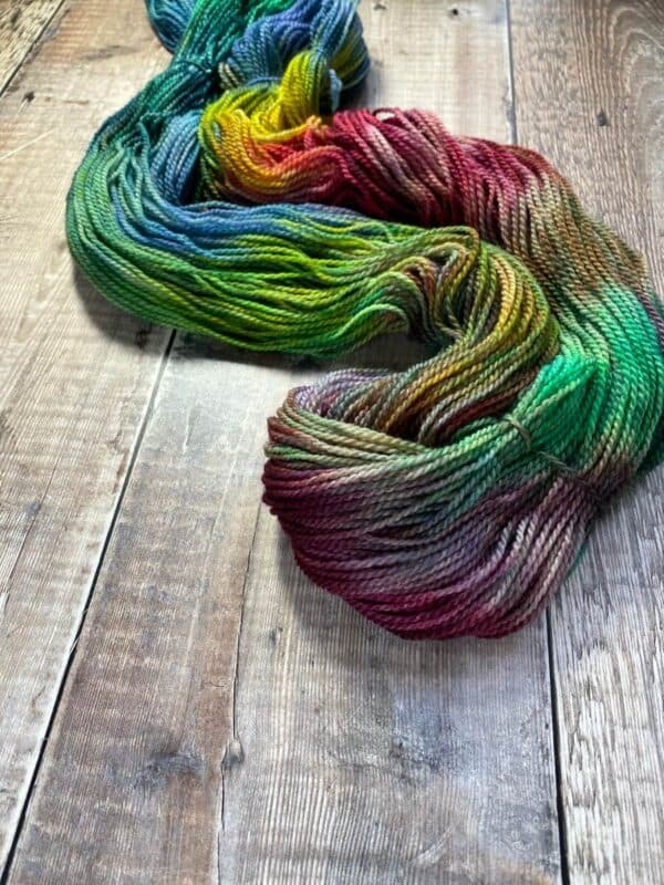 Un-skeined jewel toned rainbow yarn in fingering weight on wood table