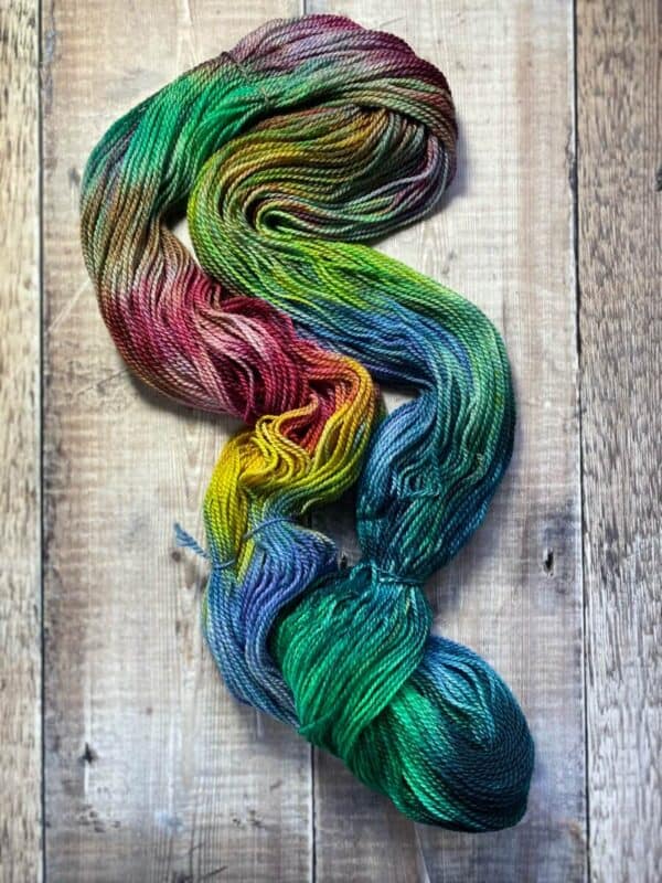 Jewel tone rainbow yarn, unstained, on wood table, flat view
